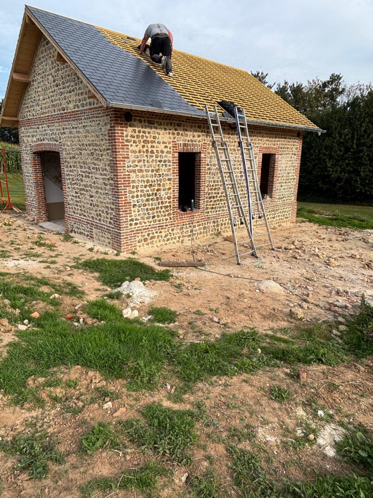 Réfection d’une toiture en ardoise sur une bâtisse normande en silex et briques.