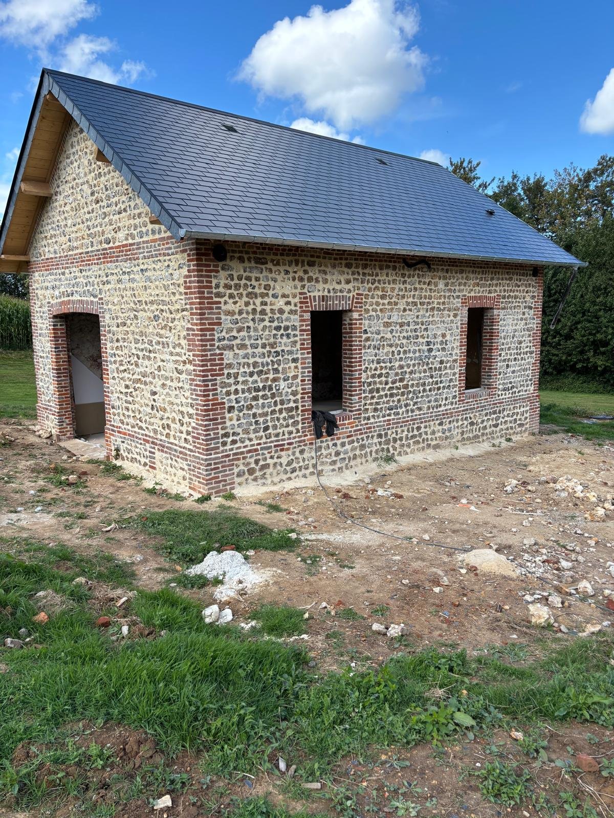 Réfection d’une toiture en ardoise sur une bâtisse normande en silex et briques.