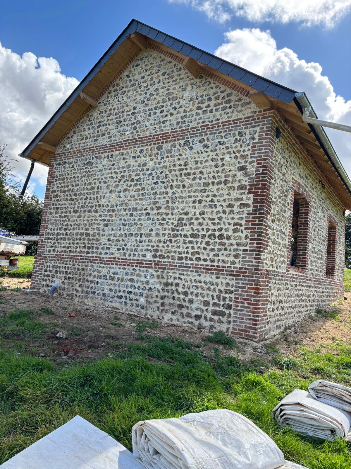 Réfection d’une toiture en ardoise sur une bâtisse normande en silex et briques.