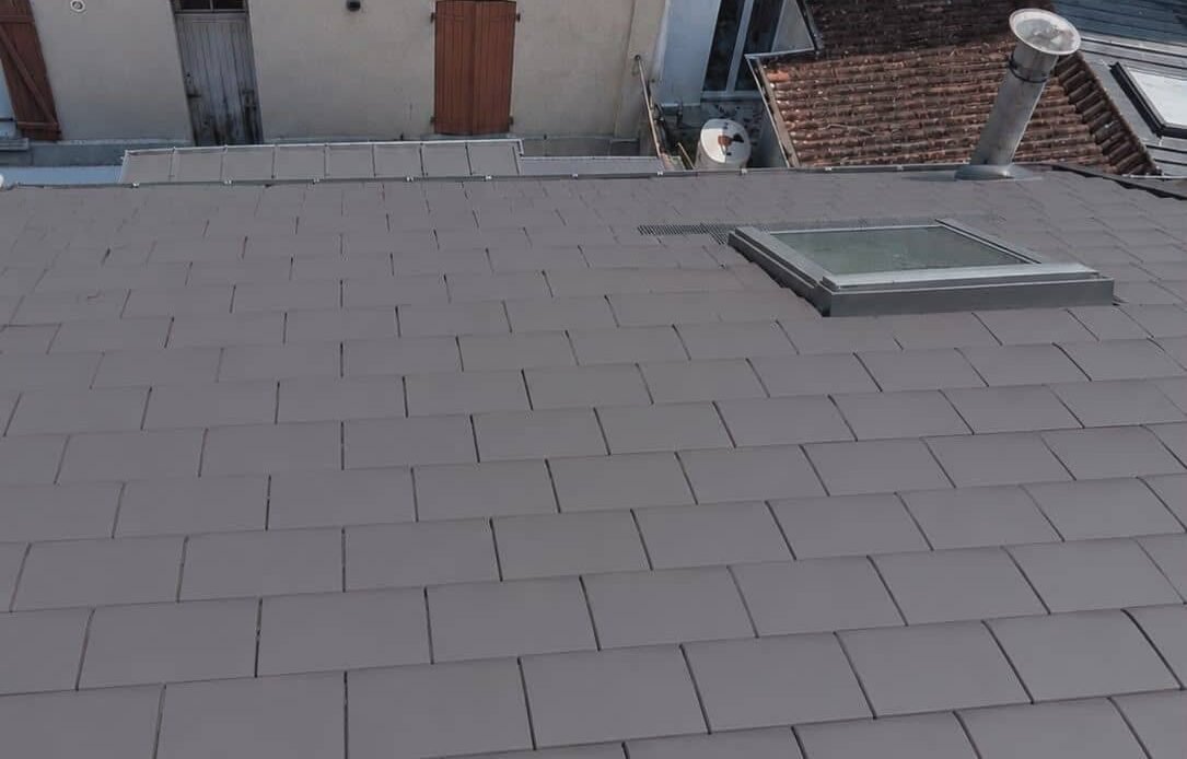 Rénovation complète d'une toiture à Rouen avec pose de tuiles plates gris anthracite, raccords d'étanchéité soignés et intégration d'une fenêtre de toit Velux.
